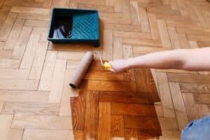 worker applying polyurethane to a hardwood floor